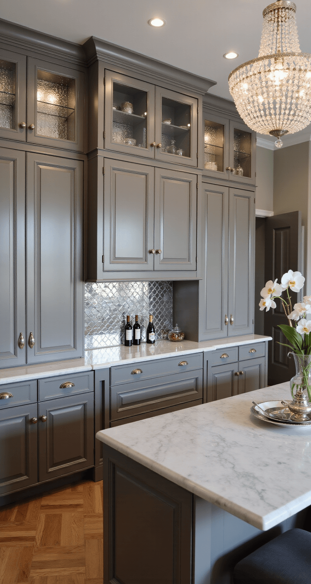 Wood Kitchen Cabinets: Your Ultimate Guide to Timeless Kitchen Design A sophisticated kitchen with grey-stained maple cabinets, a crystal chandelier casting shadows on marble countertops, polished nickel hardware, and herringbone wood floors, styled with a silver tea service, orchid arrangement, and vintage wine bottles.